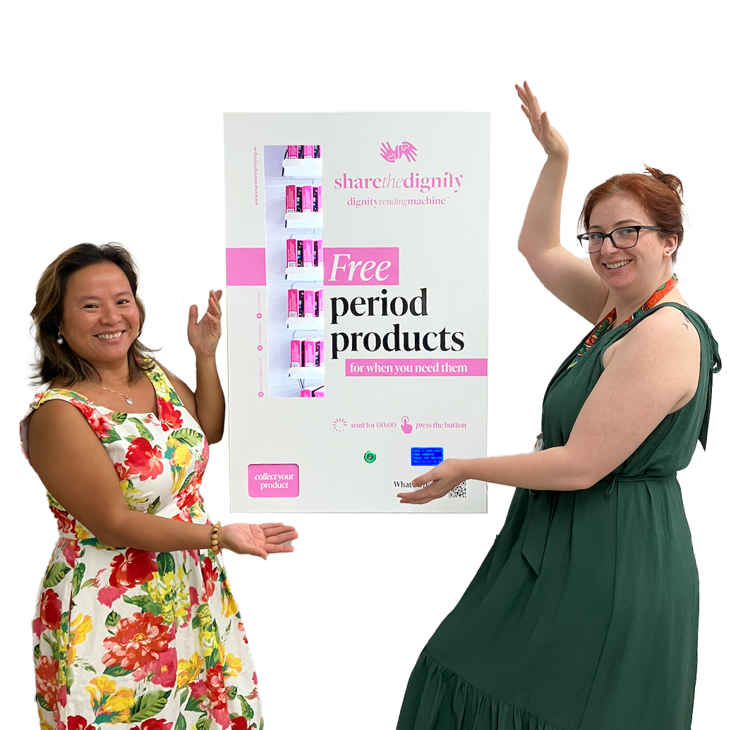 Two women pose with a newly installed Dignity Vending Machine dispensing free period products